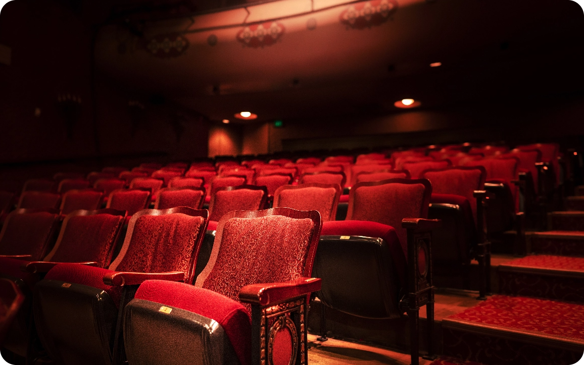 A low-lit, empty theatre with red velvet seats.
