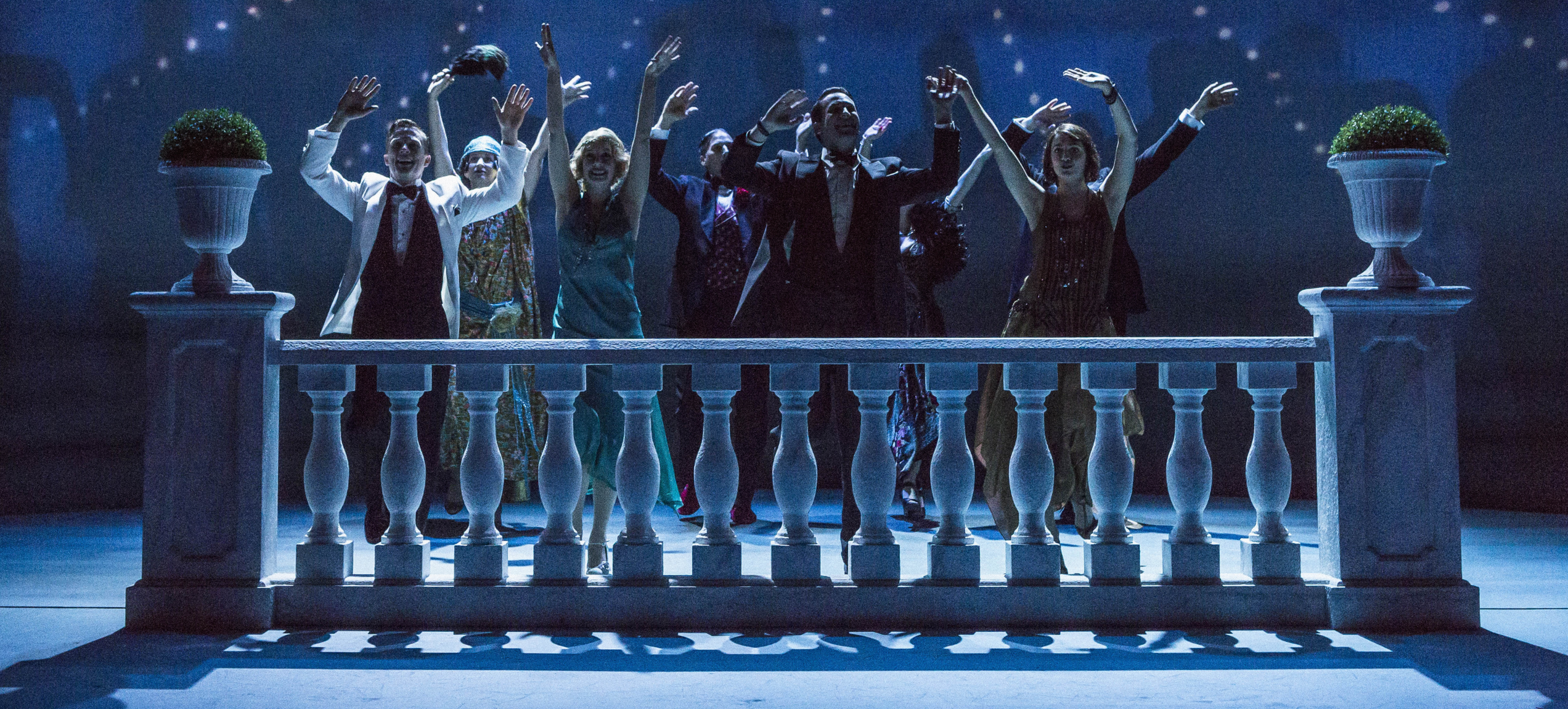 Cast members lined up on stage at the end of a show with raised hands.