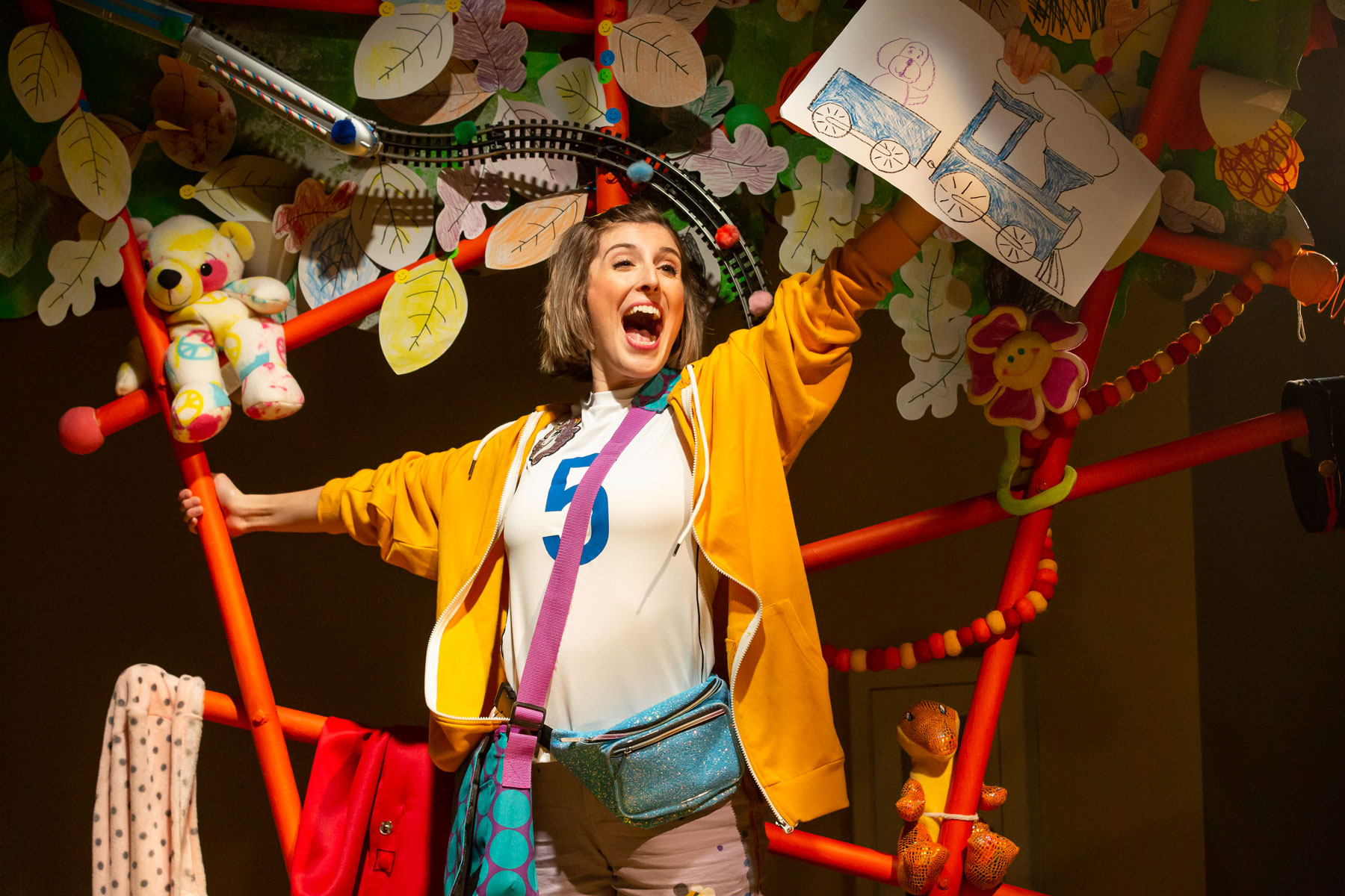 Actor in vibrant clothing standing on a platform and holding up a sign to the audience