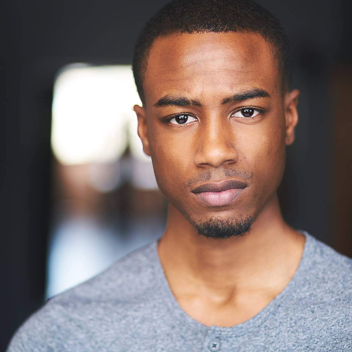Portrait of a young, African-American man standing wearing a gray shirt