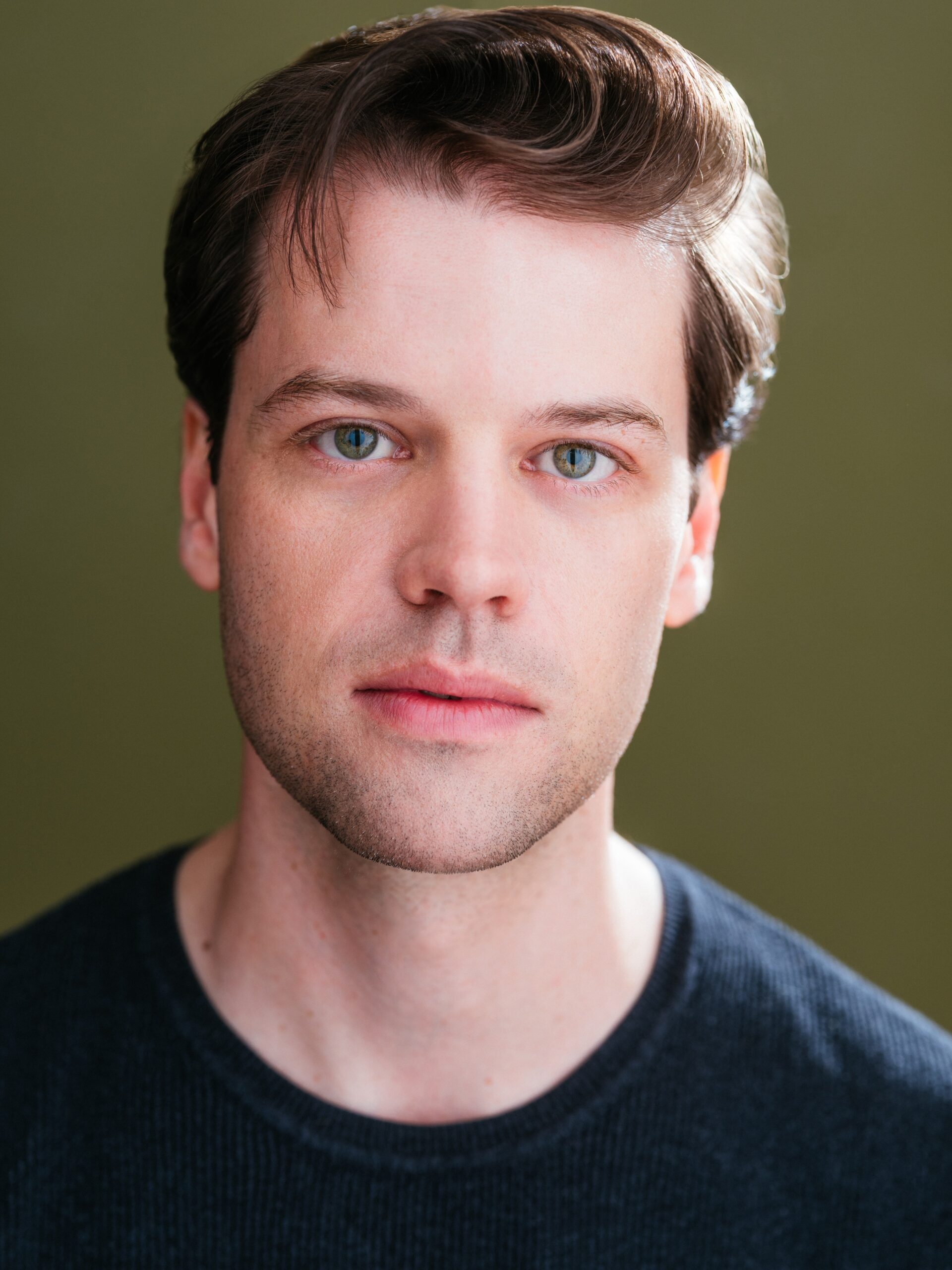 Portrait of a young, Caucasian man looking directly at the camera and wearing a black shirt on a dark background