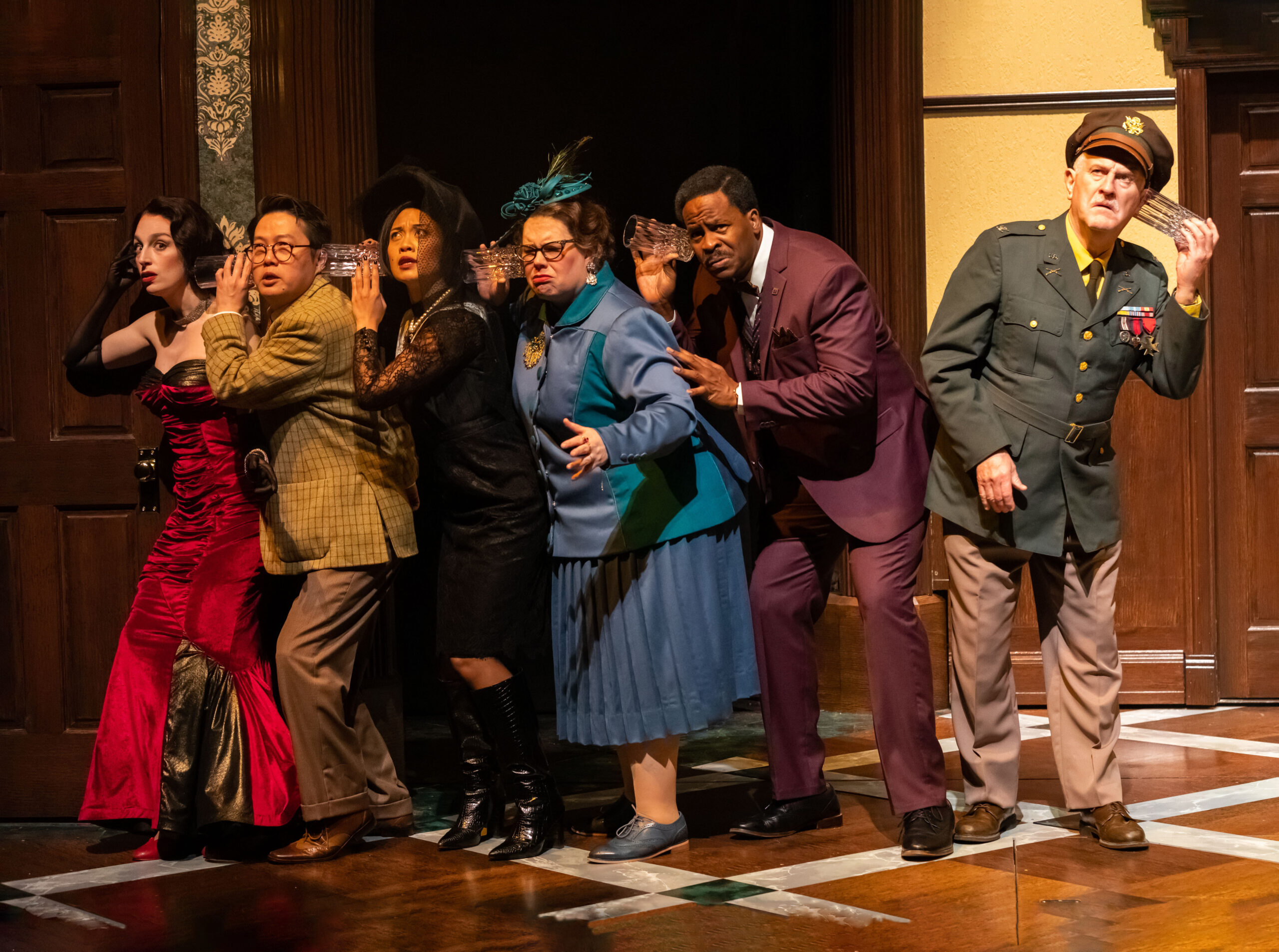 Photo of group of people all listening through a door with drinking glasses, one person listens the wrong way.
